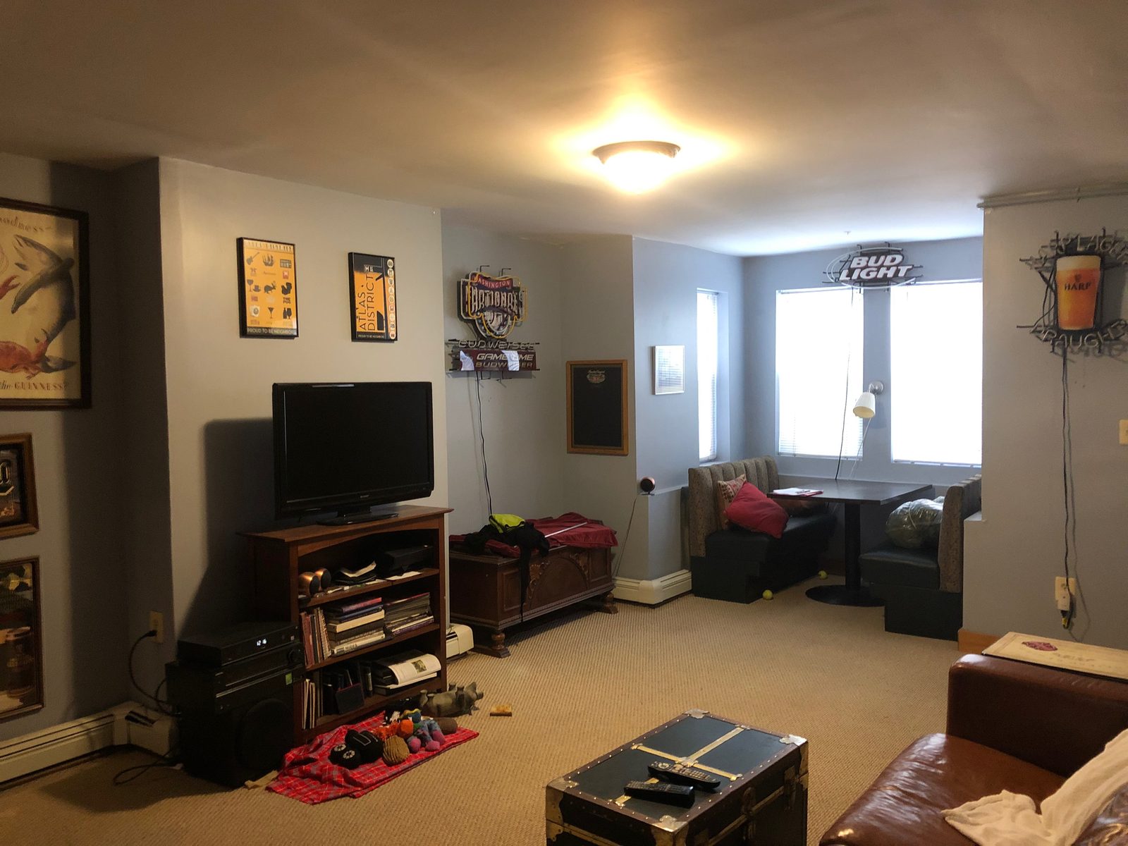 The basement rec room before, crowded with mismatched furniture and a wall of neon signs