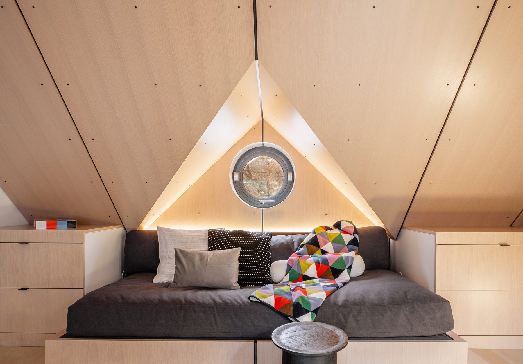 Round operable porthole window at the gable end, daybed below