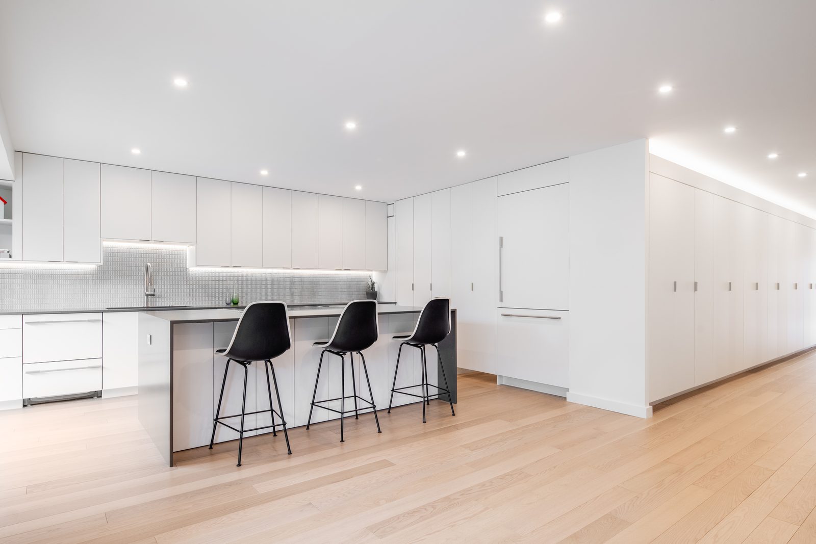 The same space now one continuous white kitchen with seating for three